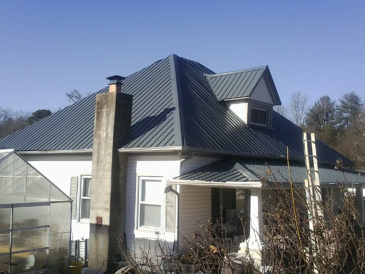 Dark blue standing seam metal roof on a white farmhouse with dormer — Slate & Tile Roof Repair by Roofing Brothers in Brooten