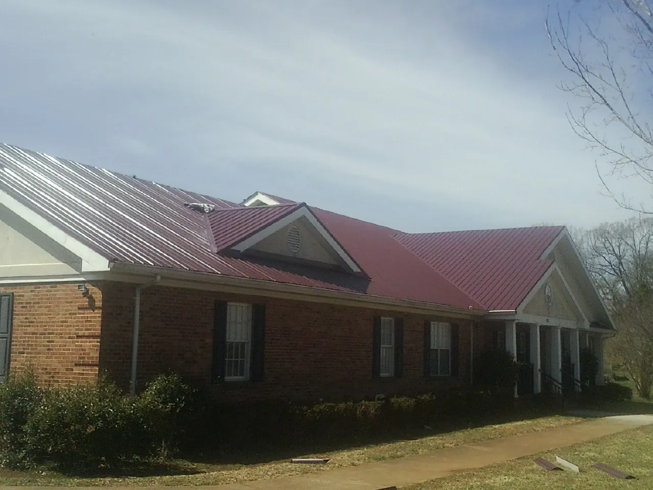 Red metal roof with gabled entries on a long brick building, from a Hail Damage Roof Repair job in Brooten