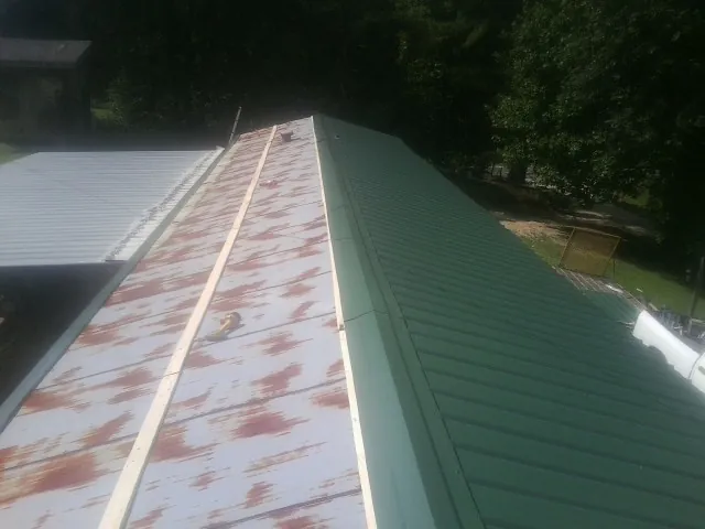 Old rusted panels beside newly installed green metal roofing — Wind Damage Roof Repair by Roofing Brothers in Brooten