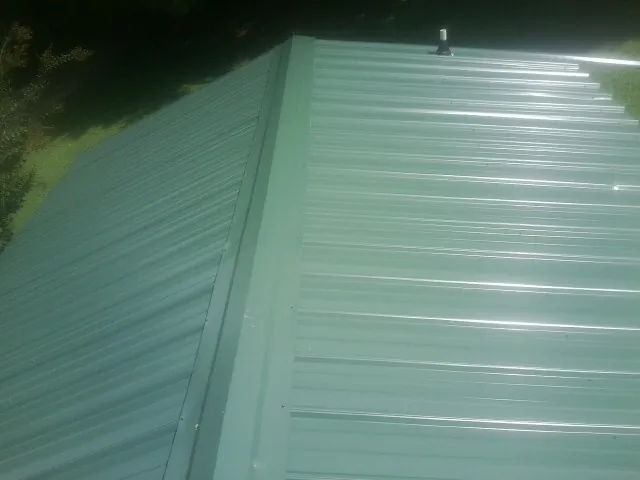 New green metal panels meeting at the ridge of a roof — Flat Roof Repair work by our crew in Brooten