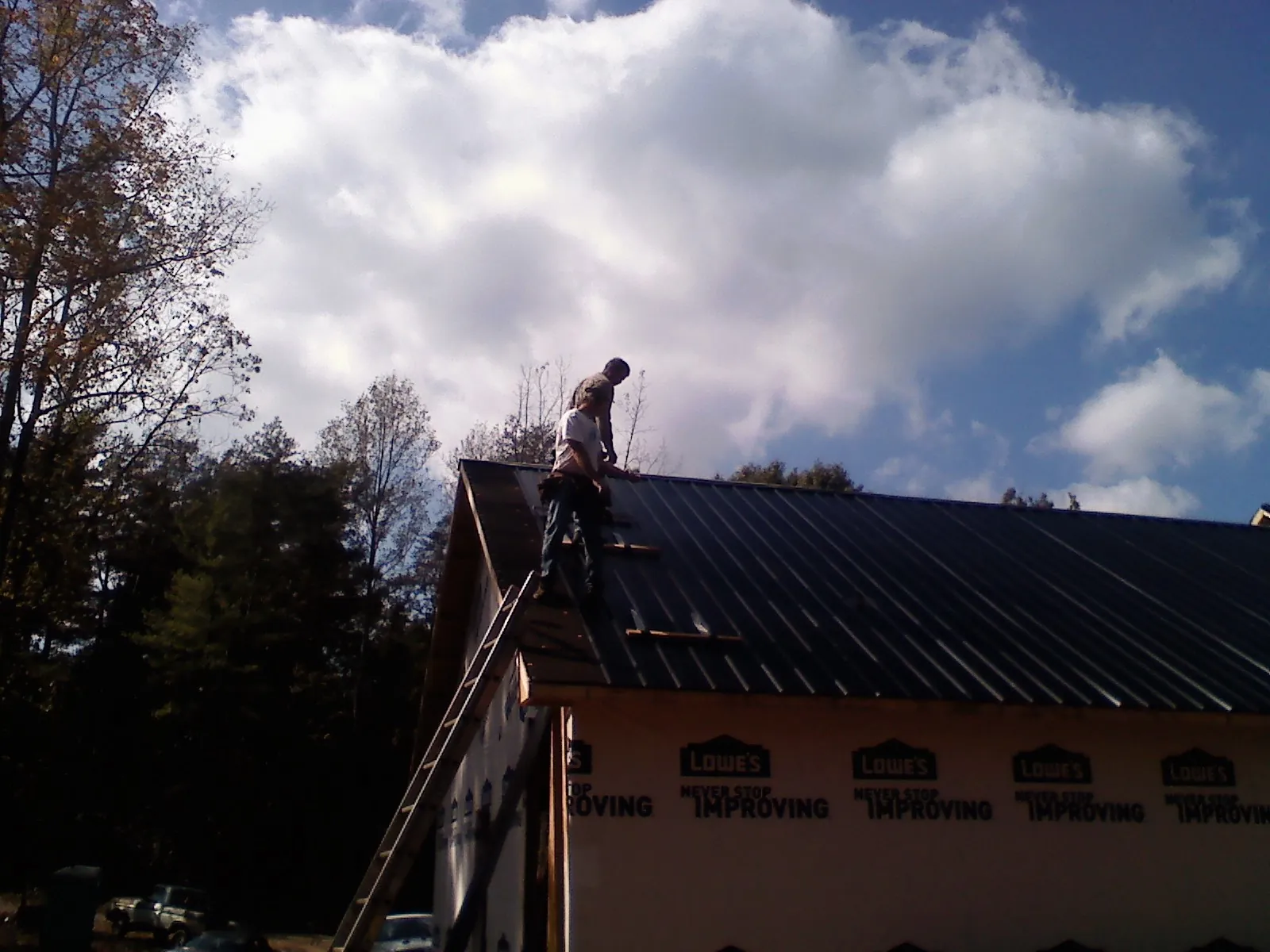 Roofer fastening dark metal panels high against a cloudy sky, from a Roof Inspection job in Brooten