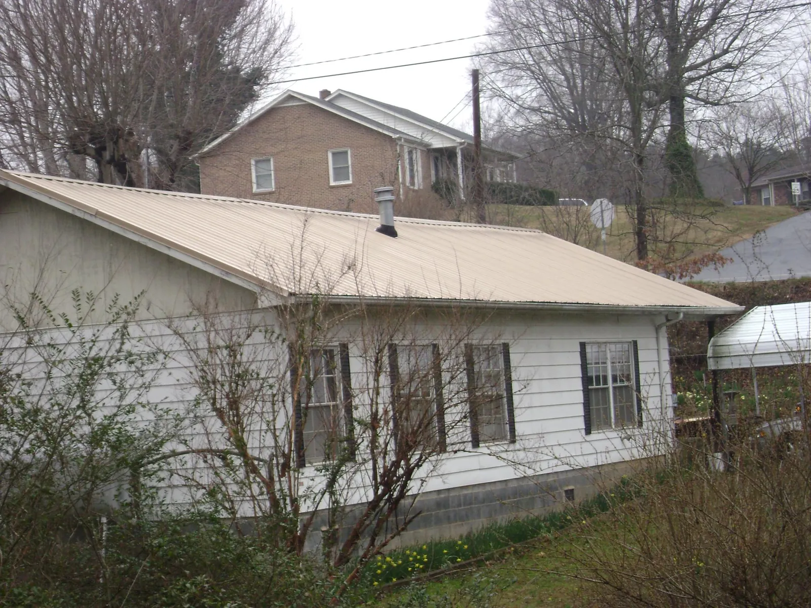 Tan metal roof on a white sided house set into a hillside — Commercial Roofing by Roofing Brothers in Brooten