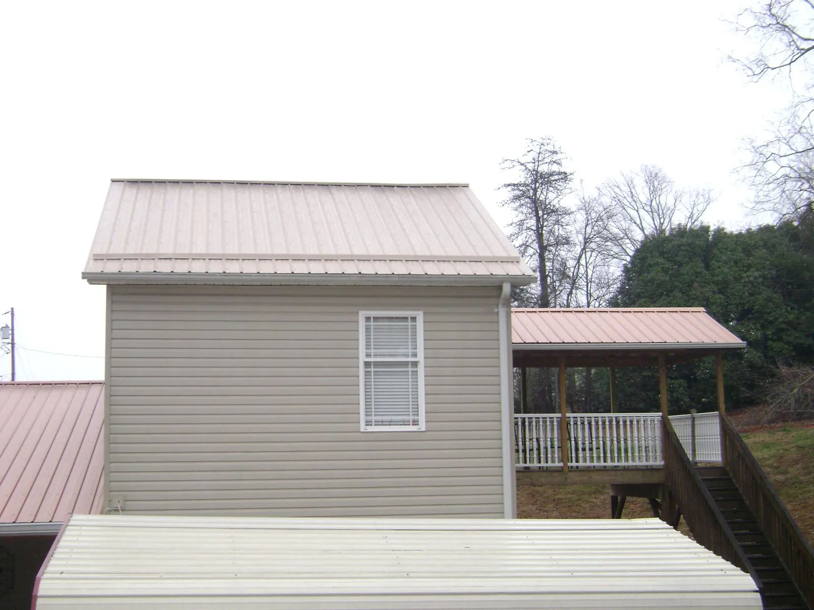 Tan metal roofs on a two story addition and attached porch, from a Roof Replacement job in Brooten